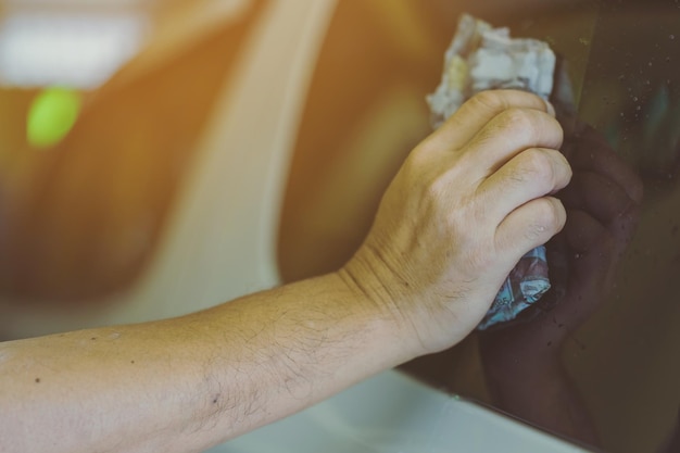 Close-up of a person using a microfiber towel to wipe down the exterior of a car, focusing on the shiny surface and the reflection in the paint.