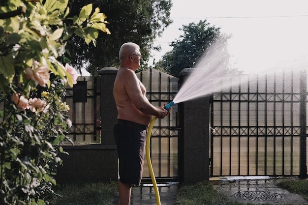 Someone is using a hose with a spray nozzle to rinse off the exterior of a gray car. The car is parked in a driveway with a house in the background. The focus is on the water running off the car, removing dirt and debris.