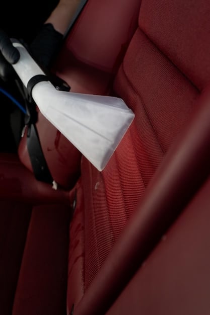 Close-up shot of a car seat with a significant stain being treated with a specialized stain remover. The focus is on the application of the cleaning product and the detailing on both the stain and the surrounding fabric.