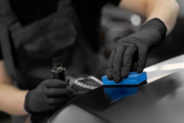 A professional car detailer carefully applying wax to a car's surface with an applicator pad. The detailer is wearing gloves and using proper techniques.