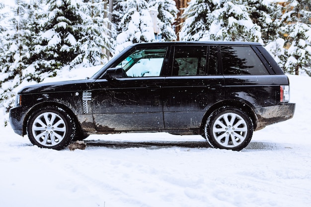 A side view of a black sedan parked in a driveway covered with light snow. The car is visibly clean, and the focus is on its lower panels, suggesting rust protection.
