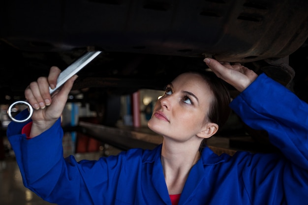 A mechanic inspecting a car's paint under bright shop lights, using a magnifying glass to check for imperfections.