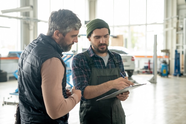A mechanic and a service advisor discussing a combination of service specials and manufacturer rebates with a car owner present, emphasizing transparent communication and informed decision-making for vehicle maintenance.