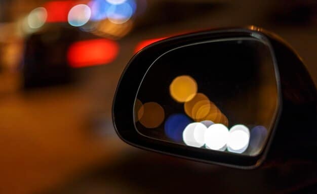A close-up of a car's side mirror with a small indicator light illuminated, representing an active blind spot monitoring system detecting a vehicle in the adjacent lane. The image should be sharp and clear, demonstrating the BSM feature in action.