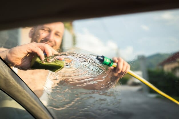 A person rinsing a car with a hose. The water is sheeting off the surface, indicating a thorough rinse. The person is using an adjustable nozzle to control the water pressure, ensuring all soap residue is removed from the car's surface.