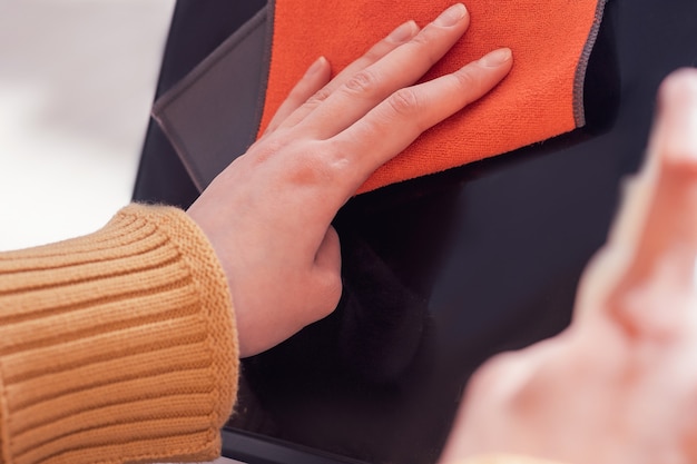 A close-up shot of a hand gently wiping a car's surface with a plush microfiber cloth. The cloth is visibly lifting dirt and grime, revealing a clean, glossy surface underneath.