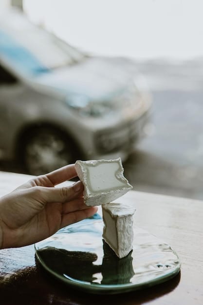 A hand holding a clay bar with a section clearly showing the contaminants it has removed from the car's surface. The car's paint is glossy and smooth where the clay bar has been used.