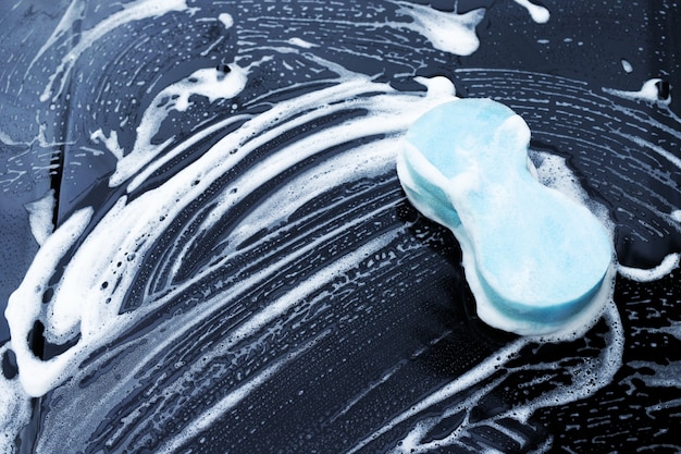 A soapy wash mitt gently cleaning the surface of a car, highlighting the two-bucket method in action to prevent scratches and swirl marks.