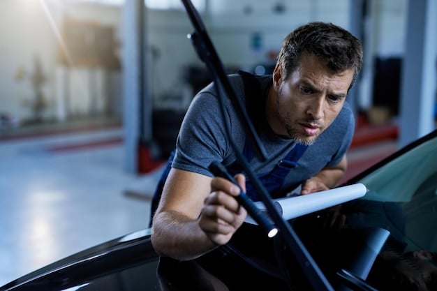 A shot of a mechanic holding a windshield wiper blade, inspecting it for wear and tear. The background shows a variety of different wiper blades on a shelf, indicating a wide selection. The image conveys the importance of choosing the correct type of wiper blade.