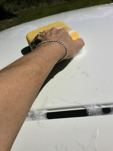 A person's hands shown installing a new windshield wiper blade onto the wiper arm, with a focus on the locking mechanism. The background is blurred, emphasizing the close-up of the installation process.