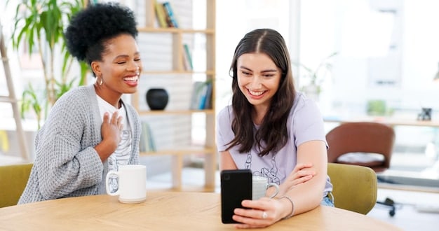 Two friends sitting at a table, one showing the other their phone with the referral screen open, smiling and discussing the benefits of the service and how to sign up.