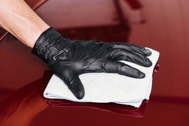Man wearing gloves is applying car wax on a car panel with a foam applicator, parked inside his garage.