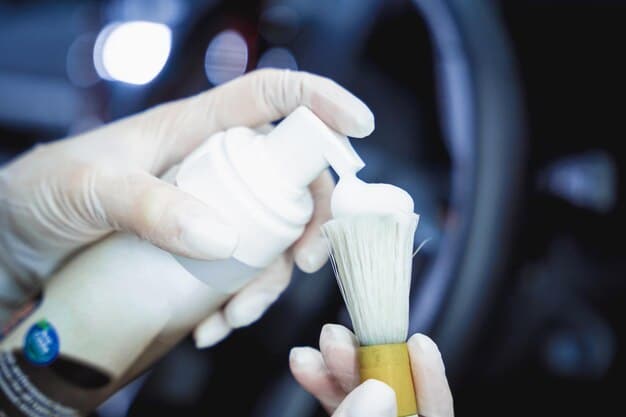 A medium shot of a person using a small brush and detailing spray to clean the air vents in a car's dashboard. The focus is on the precision and attention to detail required for effective interior car detailing.