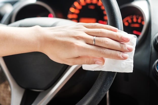 A close-up of a person using a disinfecting wipe to clean a car's steering wheel. The focus is on the importance of sanitizing frequently touched surfaces to maintain a hygienic car interior.